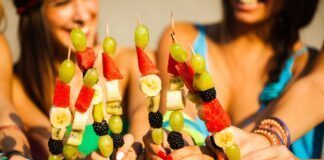 ragazze tengono in mano spiedini di frutta
