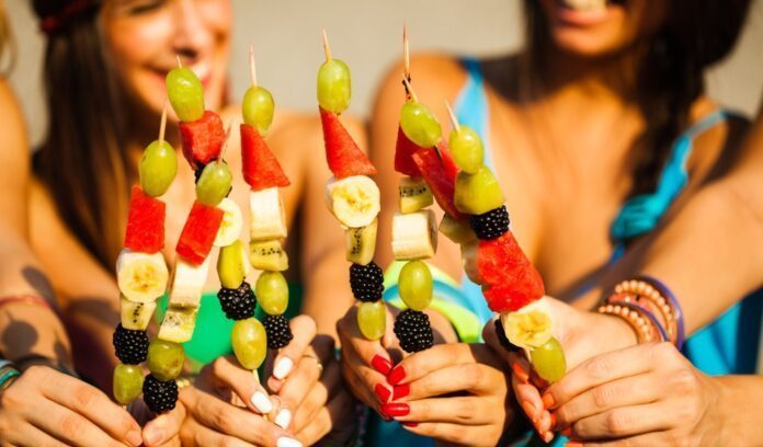 ragazze tengono in mano spiedini di frutta