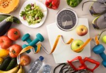 Una bilancia, degli strumenti per far esercizio come pesi ed elastici e cibo tipico della dieta mediterranea