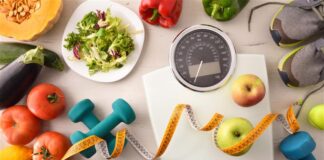 Una bilancia, degli strumenti per far esercizio come pesi ed elastici e cibo tipico della dieta mediterranea
