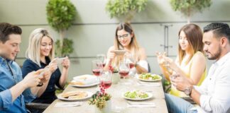 Persone che mangiano a un tavolo con il telefono in mano