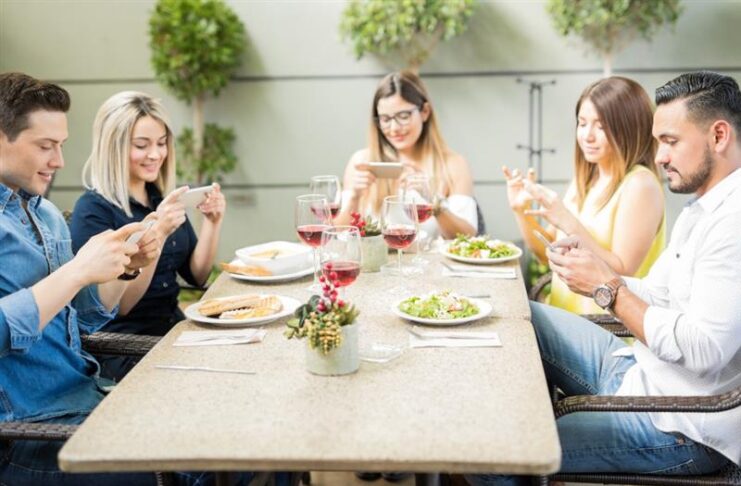 Persone che mangiano a un tavolo con il telefono in mano